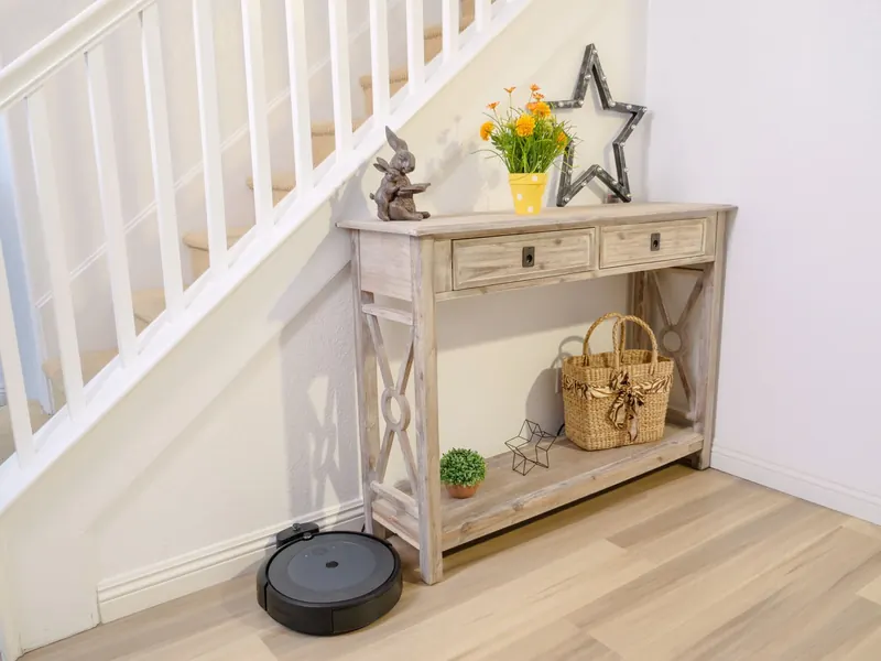Stylish home hallway with a robotic vacuum and decorative wooden table under stairs