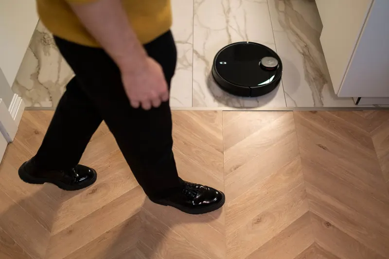 A robotic vacuum cleaner operating on a wooden floor, viewed in high angle indoor setting