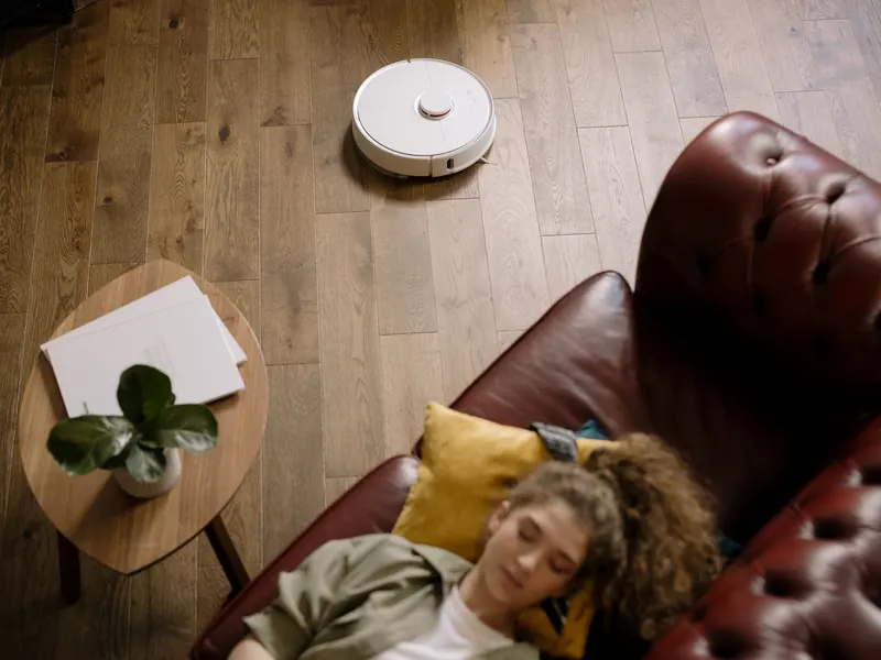 A modern living room with a robotic vacuum and a woman resting, showcasing ease and comfort