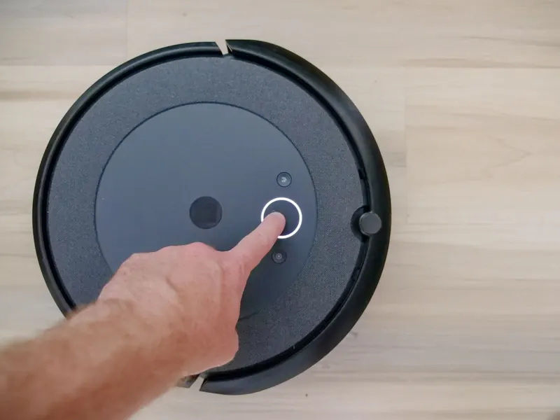Close-up of a finger pressing a start button on a robotic vacuum cleaner at home