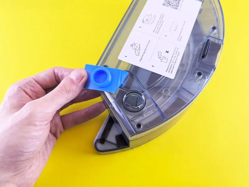 Close-up of a person holding a vacuum cleaner water tank with a yellow background