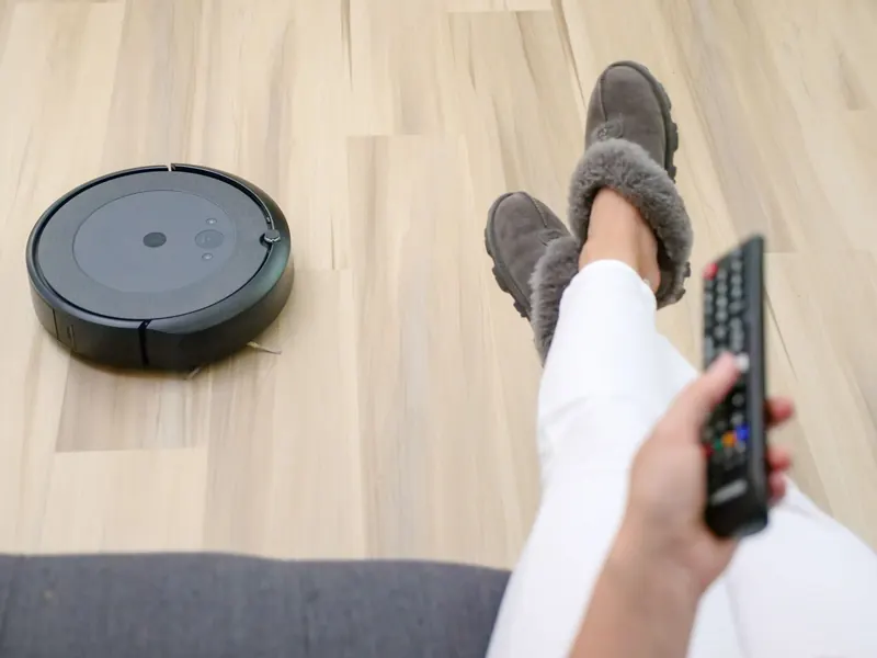 A person relaxing on a couch with a robotic vacuum cleaning the hardwood floor