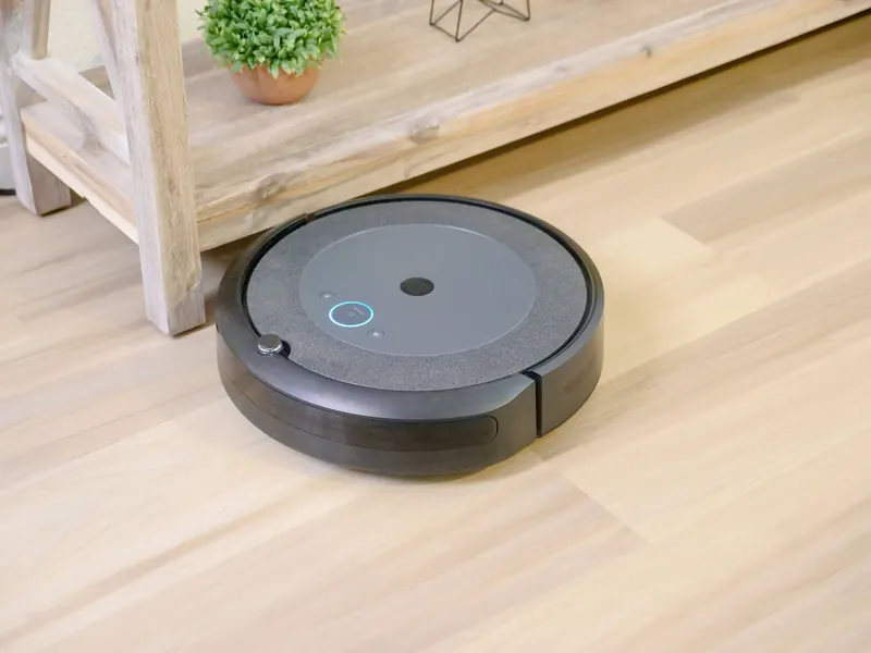 Automated robotic vacuum cleaner on hardwood floor next to plant