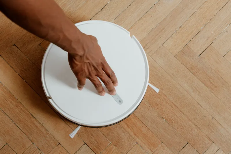 A close-up of a hand activating a robotic vacuum cleaner on a wooden floor