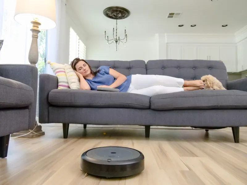 A woman relaxing on a sofa with a robotic vacuum cleaner cleaning the hardwood floor