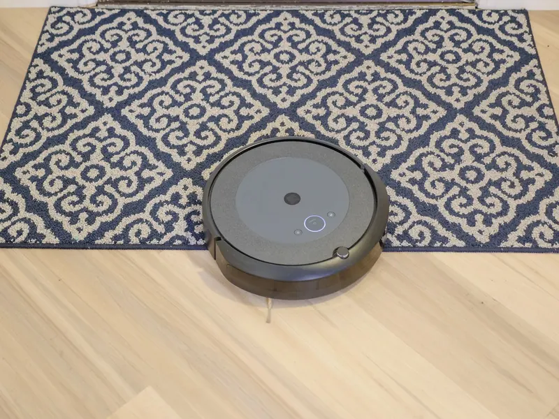 A modern robotic vacuum cleaning a stylish patterned carpet on a wooden floor