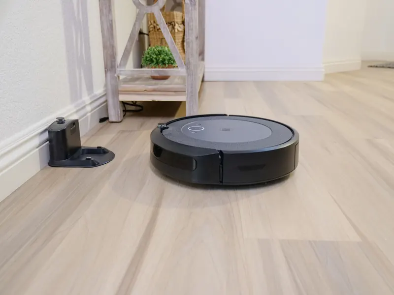 A sleek robotic vacuum navigates a clean hardwood floor beside a docking station
