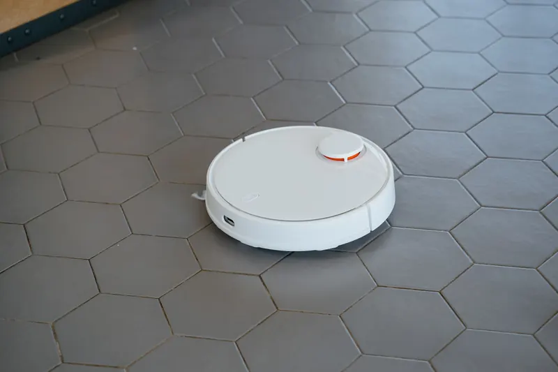 A sleek, white robotic vacuum cleaner operating on a hexagonal tiled floor